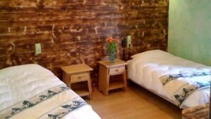 Une chambre avec deux lits, une tête de lit en bois, de petites tables de chevet en bois et un mur vert.