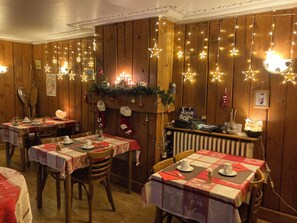 A cozy restaurant with wooden walls, star-shaped string lights, and Christmas decorations. Tables are set with white tablecloths and red napkins. - Hôtel La Marmotte (Gerardmer)