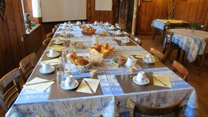 Un espace repas avec de longues tables préparées pour le petit-déjeuner, avec du pain, des viennoiseries et des boissons.