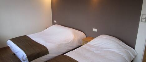 A room with two single beds, each with a wooden headboard and a brown blanket. There are two wall-mounted lights above the beds.