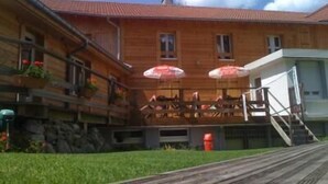 Un bâtiment en bois avec un toit rouge, des tables à l’extérieur sous des parasols et un escalier menant à un deuxième étage.