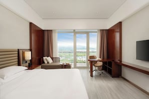 Habitación de hotel con cama, escritorio, silla, televisor y vistas a la ciudad.