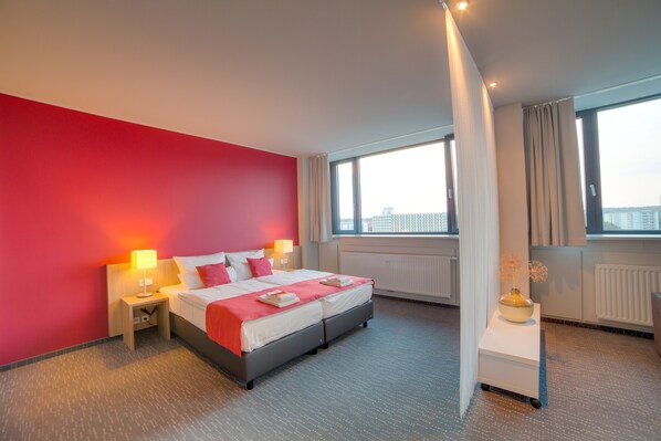 Una habitación de hotel moderna con una cama grande, una mesita de noche con lámpara, una ventana con cortinas y un radiador.