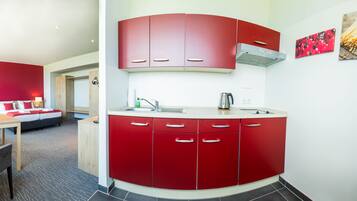 Una habitación de hotel moderna con cocina roja, una cama con ropa de cama roja y un comedor.