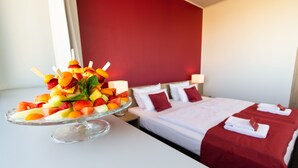Una habitación de hotel con una cama, una mesita de noche con una bandeja de frutas y una pared roja.
