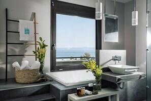 A modern bathroom with a bathtub, sink, and a view of the sea.
