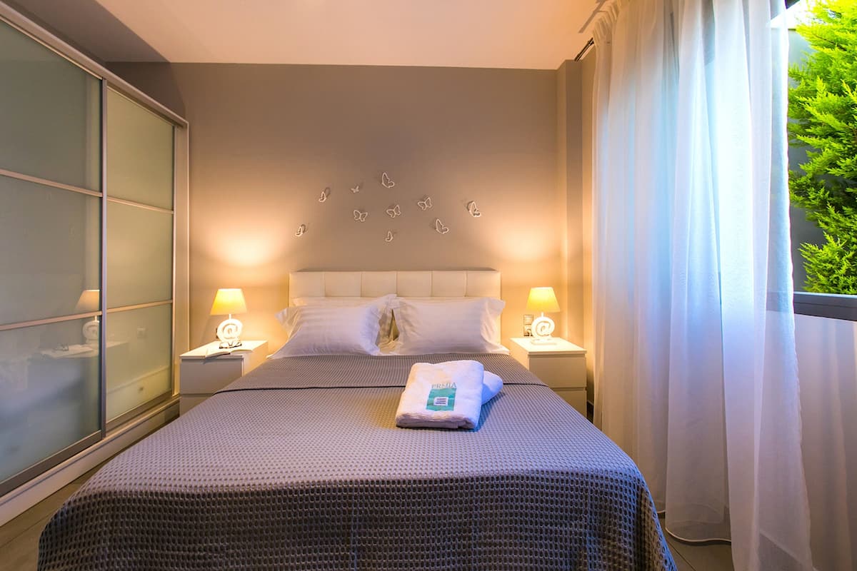 A neatly made bed with a folded towel, two bedside lamps, and a wall with butterfly decals.