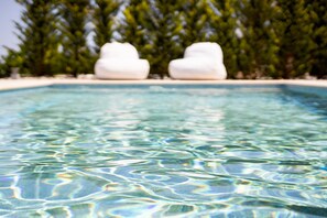 A clear swimming pool with two white, cloud-shaped sculptures on the edge.