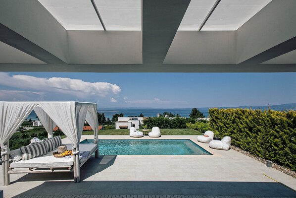 A modern outdoor pool area with a canopy bed and lounge chairs, overlooking a scenic view.