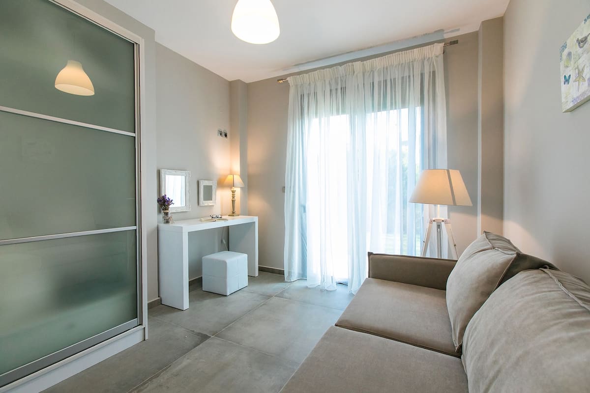 A modern hotel room with a sofa, a desk, and a large window with curtains.
