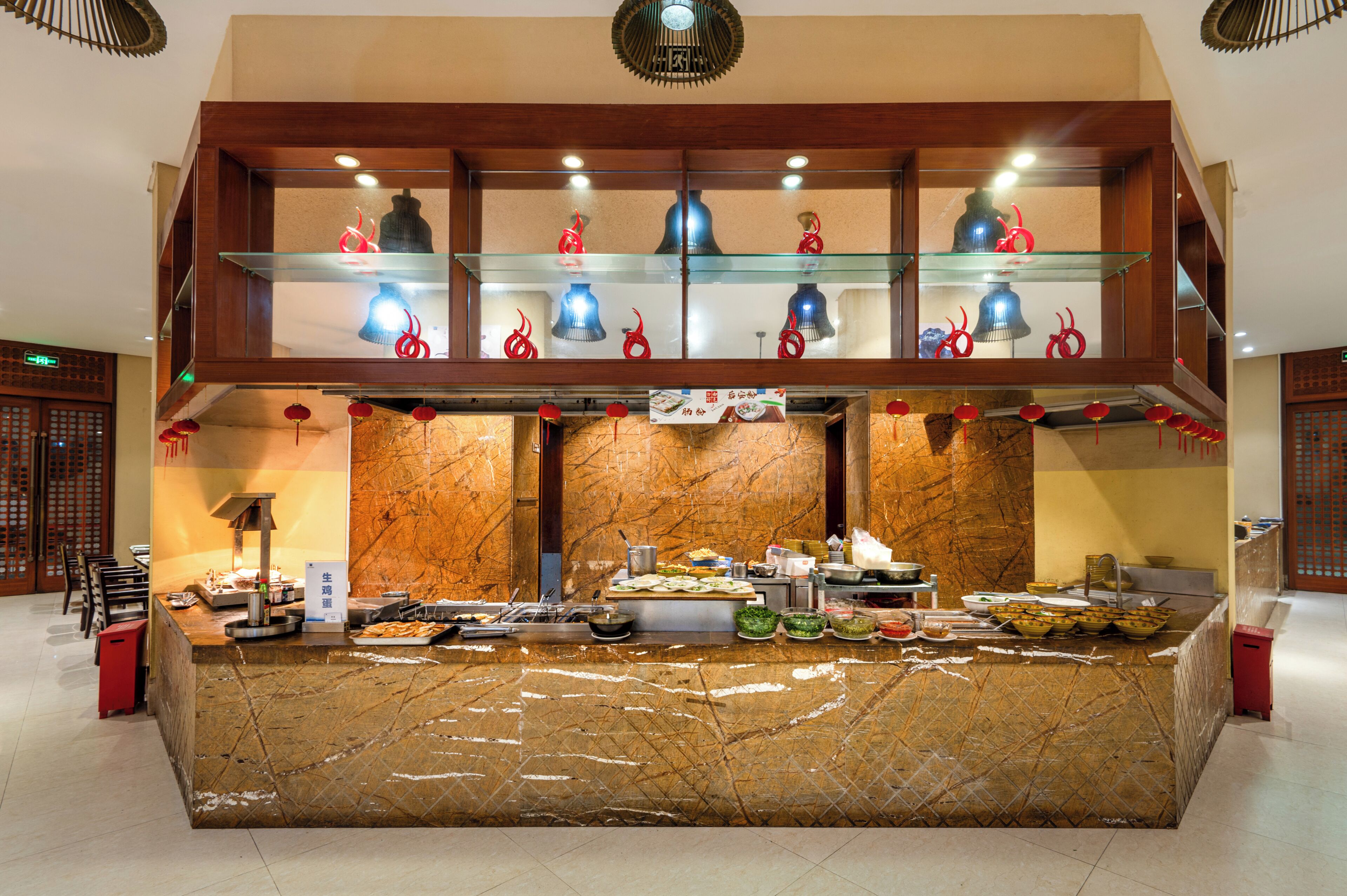 A buffet setup with a marble counter, overhead glass shelves with decorative items, and a traditional ceiling fan.