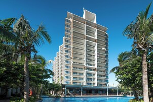 Ein mehrstöckiges Hotel mit Balkonen, umgeben von Palmen und einem Swimmingpool.