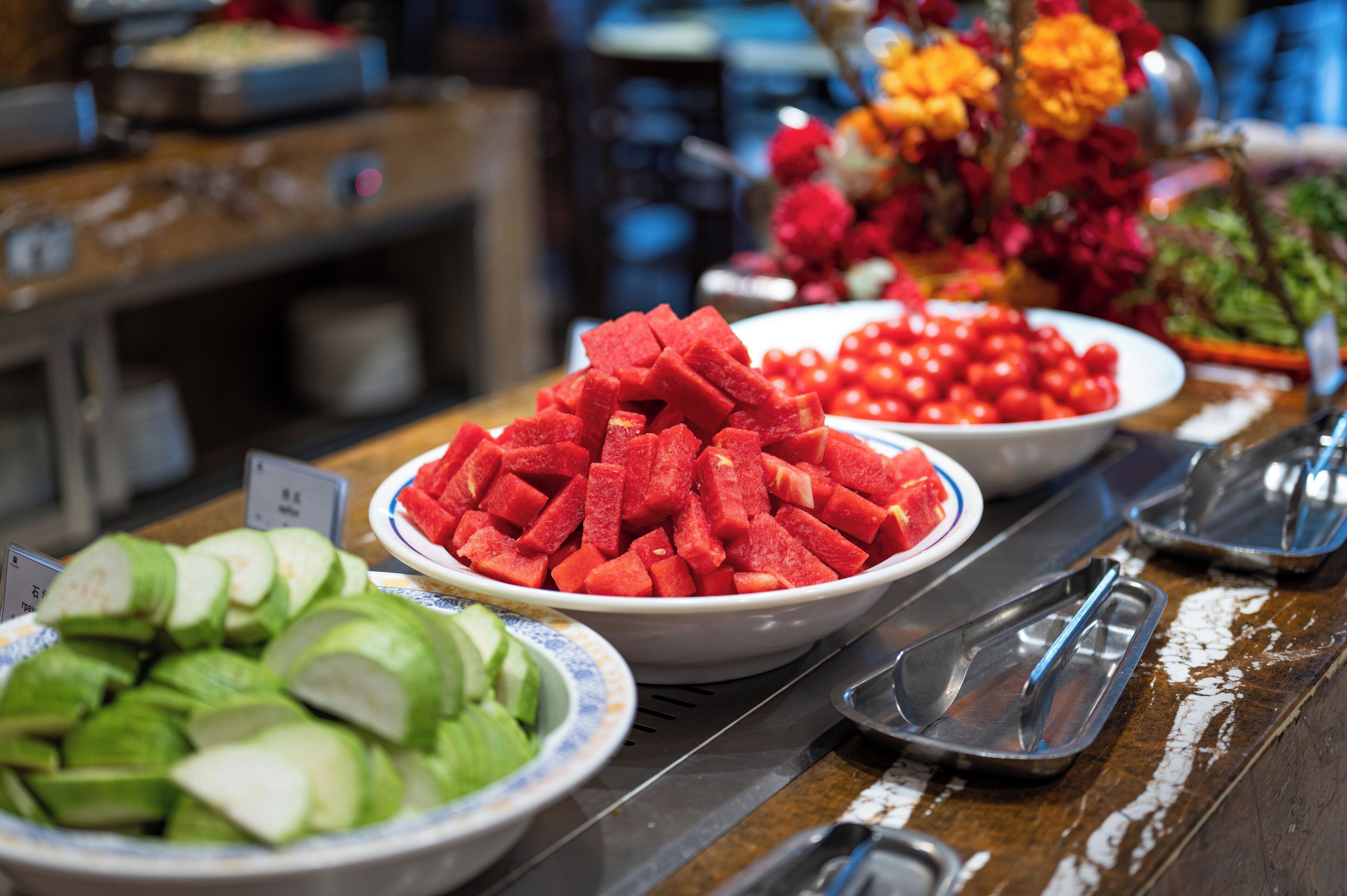 Een buffet met diverse soorten eten, waaronder watermeloen, komkommers en een schaal rode tomaten.