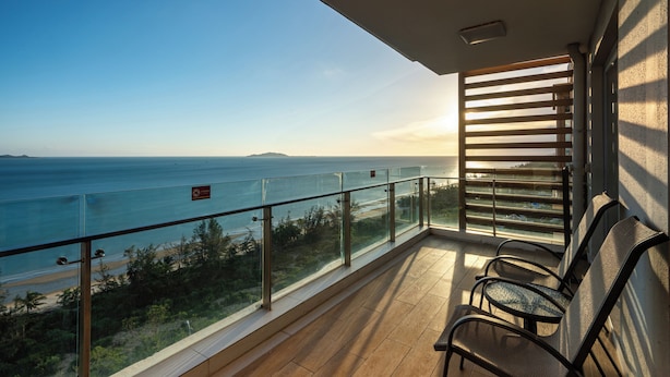 Un balcon avec vue sur la mer, une balustrade en verre et deux chaises.