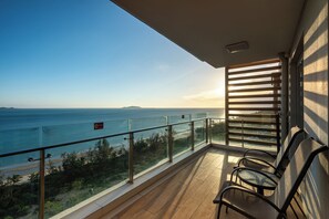 Un balcone con vista sul mare, ringhiera in vetro e due sedie.