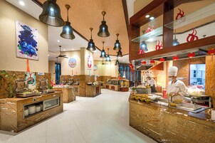 Zona de bufé con varias estaciones de comida, iluminación colgante y un chef preparando alimentos.