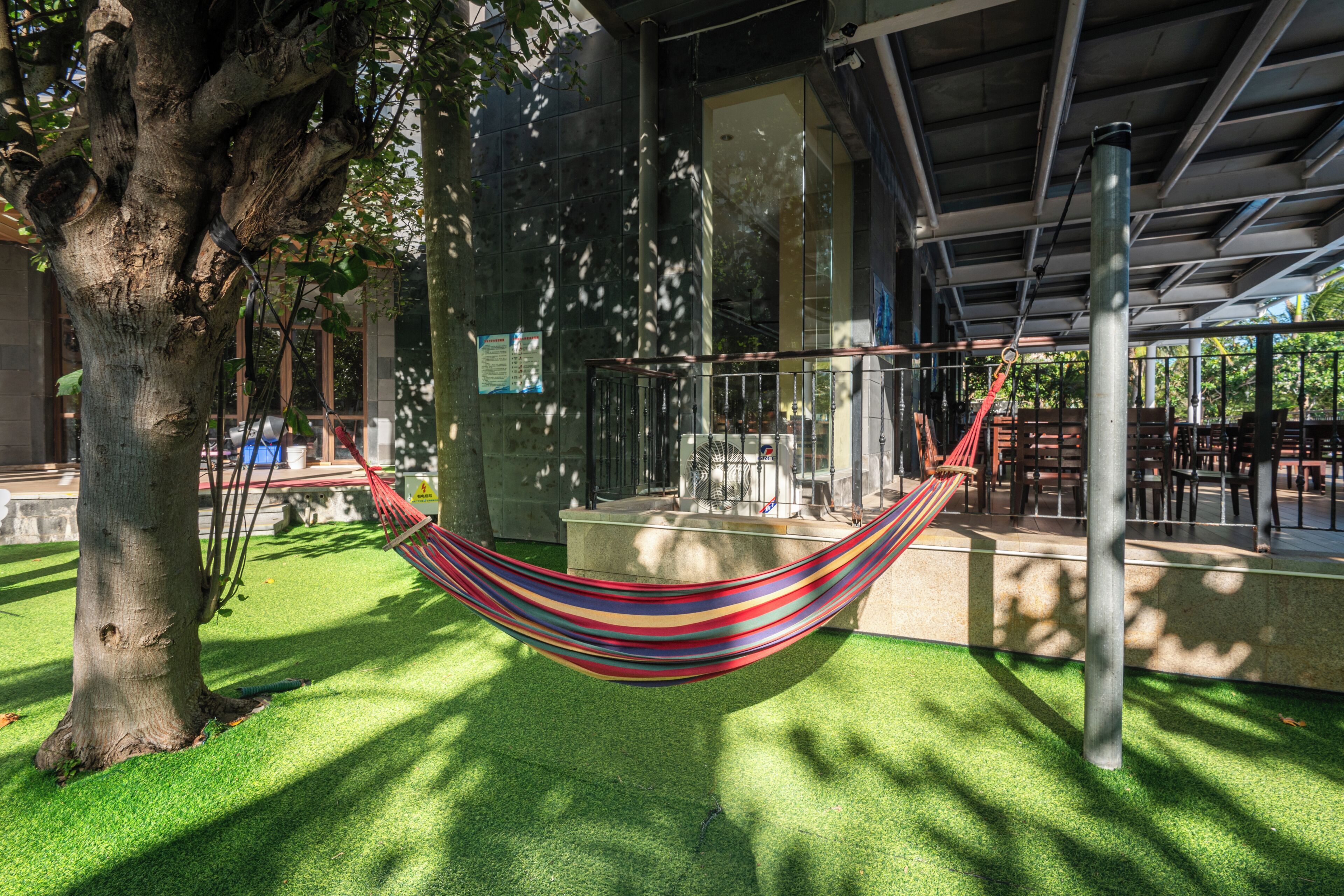 A hammock between trees, a covered seating area, and a building with large windows.