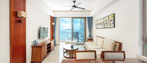 A modern hotel room with a balcony, a sofa, a coffee table, and a television.