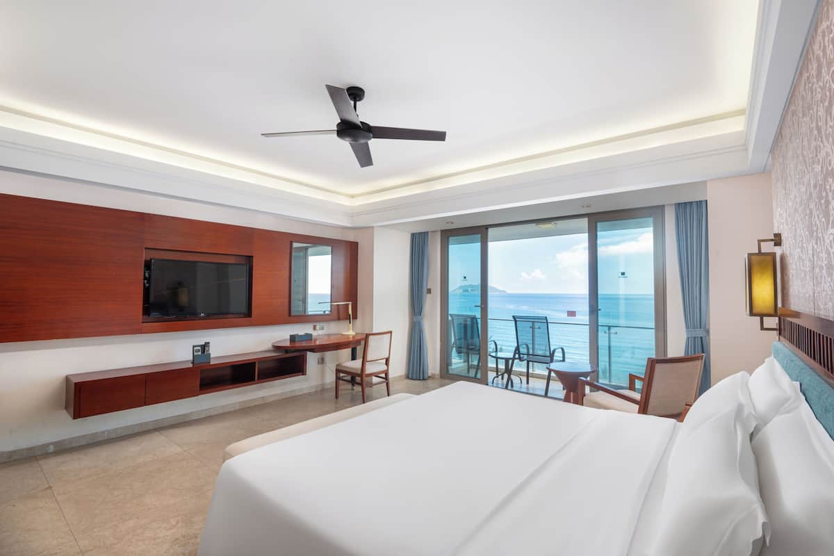 Una camera d'albergo con un letto, TV, scrivania e un balcone con vista sul mare.
