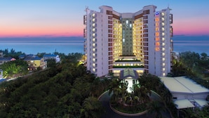 Un hôtel à plusieurs étages doté d’un atrium central, entouré de verdure et offrant une vue sur la mer.