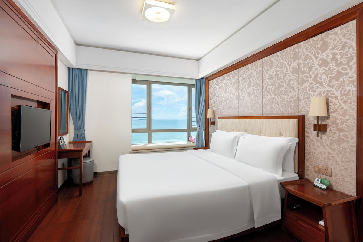 Una camera d'albergo con un letto grande, una televisione, una finestra vista mare e un pavimento in legno.