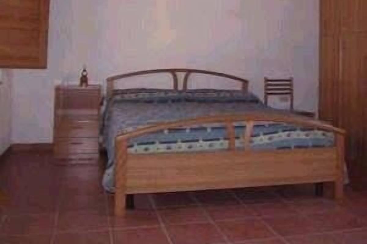 Een slaapkamer met een houten bed, een nachtkastje en een stoel.