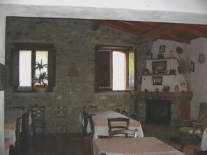 Een rustieke eetkamer met een stenen muur, houten balken, een open haard en een tafel gedekt voor vier personen.
