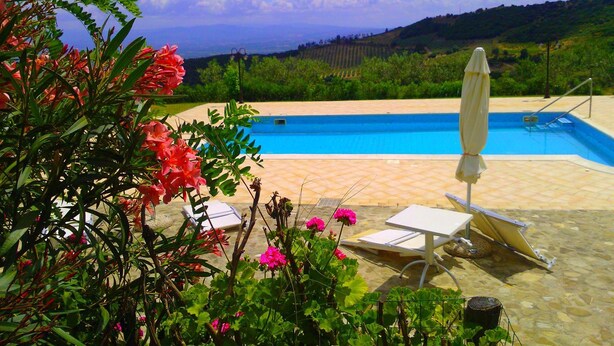 A pool area with a view of the countryside, a lounge chair, and a table. - Agriturismo San Fele (Cerchiara di Calabria)