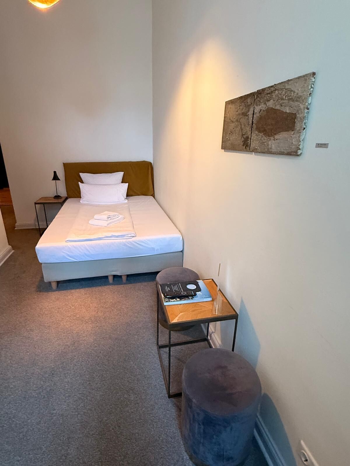 A bedroom with a bed, bedside table, lamp, and a small stool.