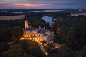 A large, castle-like building with a tower, surrounded by trees and a lake. - Hotel Schloss Reichenow (Reichenow-Möglin)