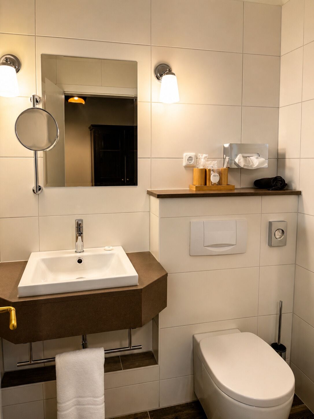 Un baño moderno con un lavabo rectangular, un inodoro, un espejo y un estante con artículos de aseo.