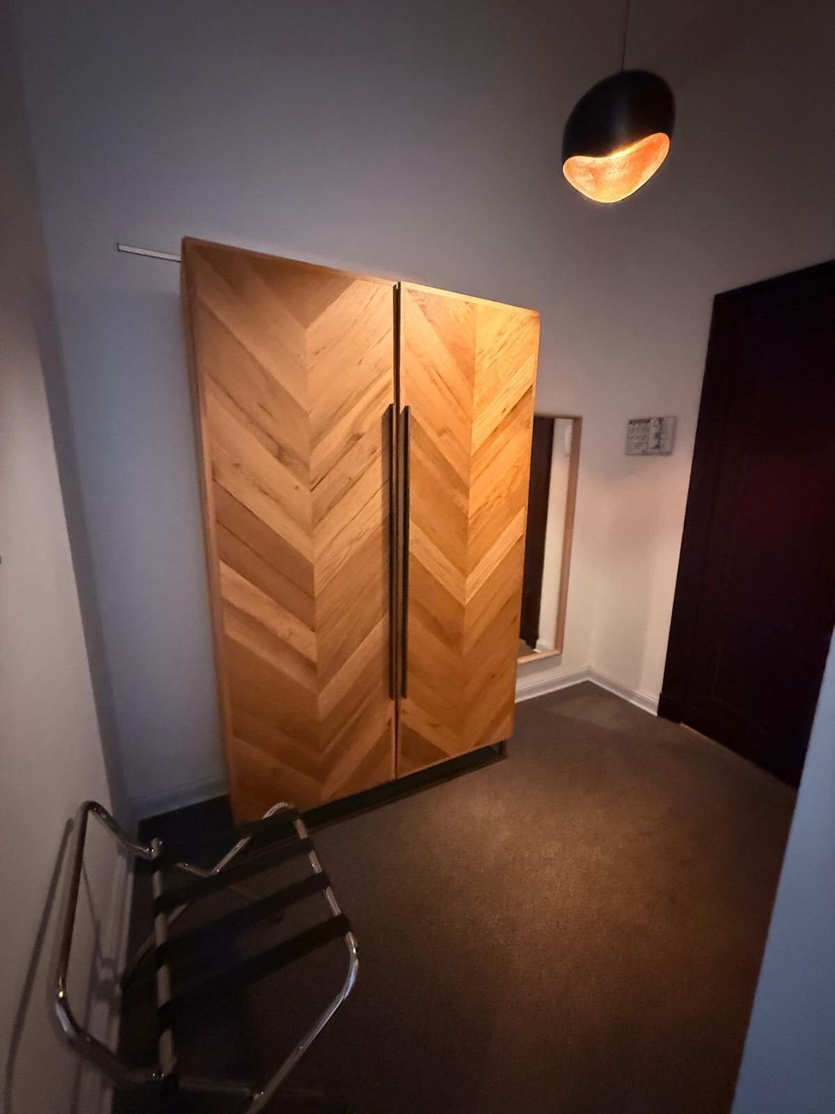 Une pièce avec une armoire à motifs en chevrons, un luminaire suspendu et une chaise.