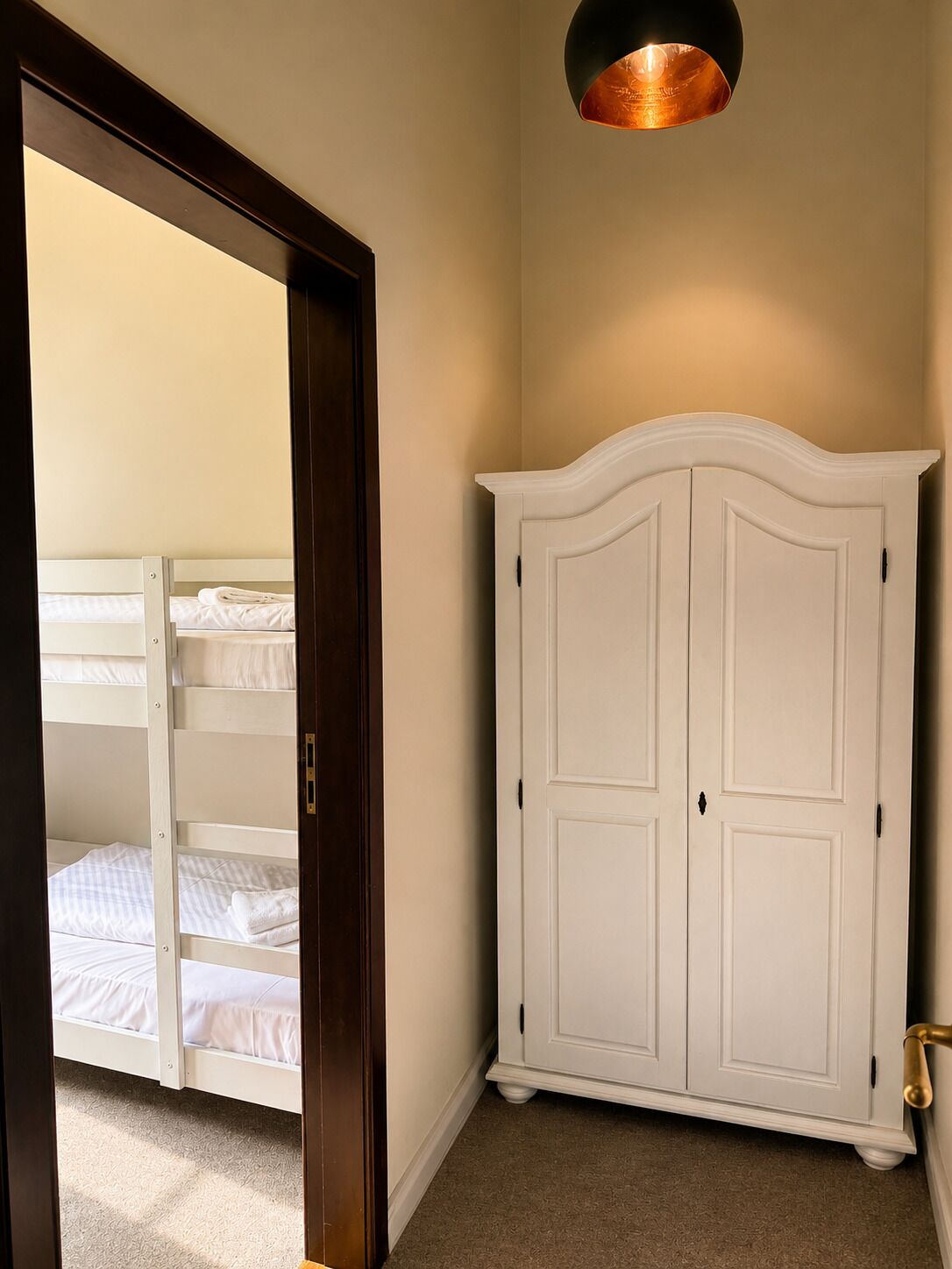 A bedroom with a bunk bed, a white wardrobe, and a ceiling light fixture.