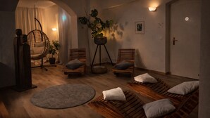 A modern spa room with wooden loungers, a hanging chair, and a large potted plant.