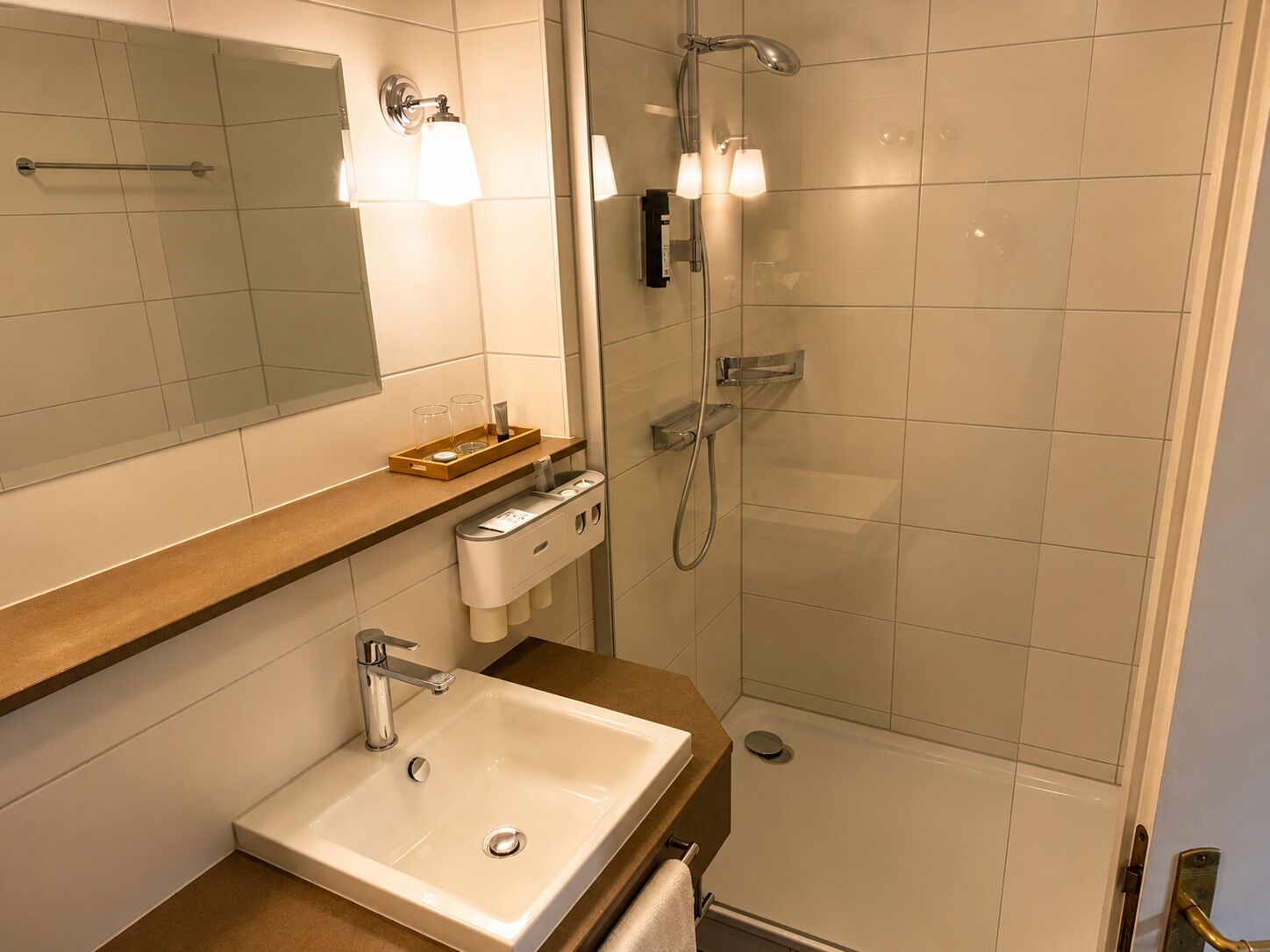 Un baño moderno con lavamanos, espejo, toallero, ducha y repisas con artículos de aseo.