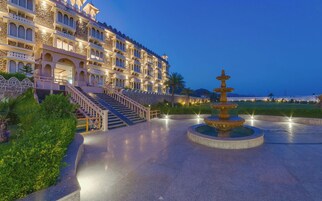Un hotel de varios pisos con una entrada imponente, una fuente central y un área exterior bien iluminada.