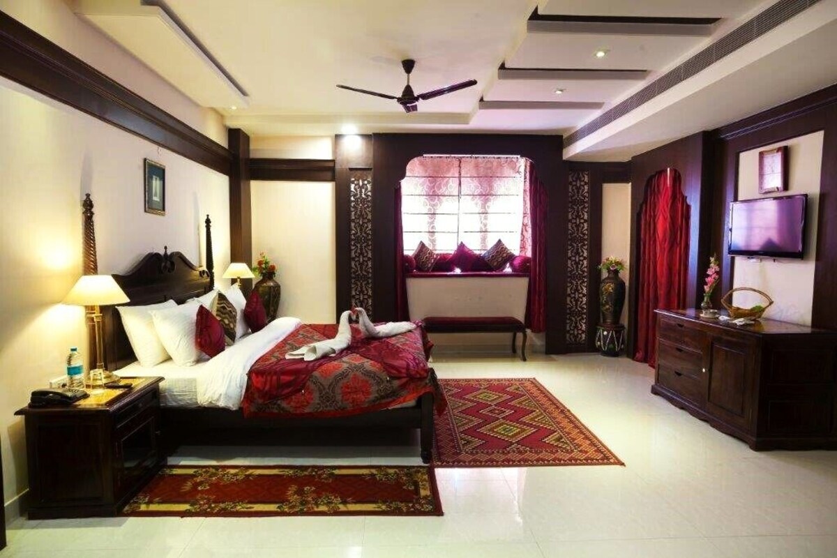 A hotel room with a bed, a desk, a TV, a window with curtains, and a ceiling fan.