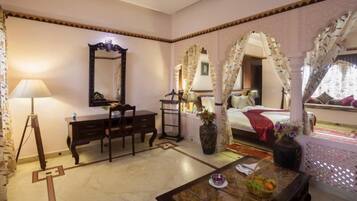 A hotel room with a bed, a desk, a chair, a lamp, and a vase with flowers.