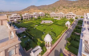 A large, multi-story hotel with a central courtyard, surrounded by lush greenery and a mountainous backdrop. - Bhanwar Singh Palace (Pushkar)