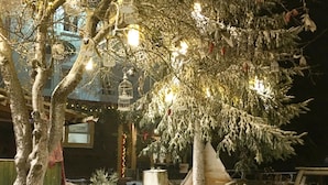 A snow-covered outdoor area with a wooden structure, lanterns, and a snow-covered tree.