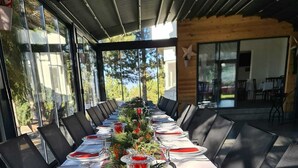 A long dining table set for a meal with chairs on both sides, decorated with greenery and red accents.