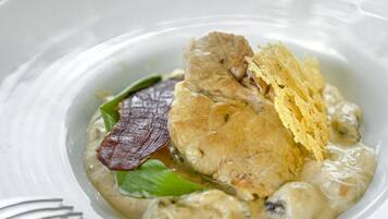 Un plato blanco con un guiso cremoso, una copa de vino blanco y un tenedor.