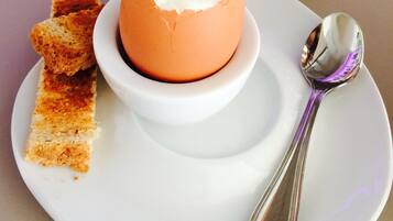 A dish with a poached egg on a white plate, accompanied by a spoon and a piece of toast.