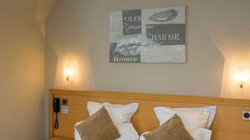 A hotel room with a large bed, two bedside tables, a chandelier, and a wall-mounted artwork.