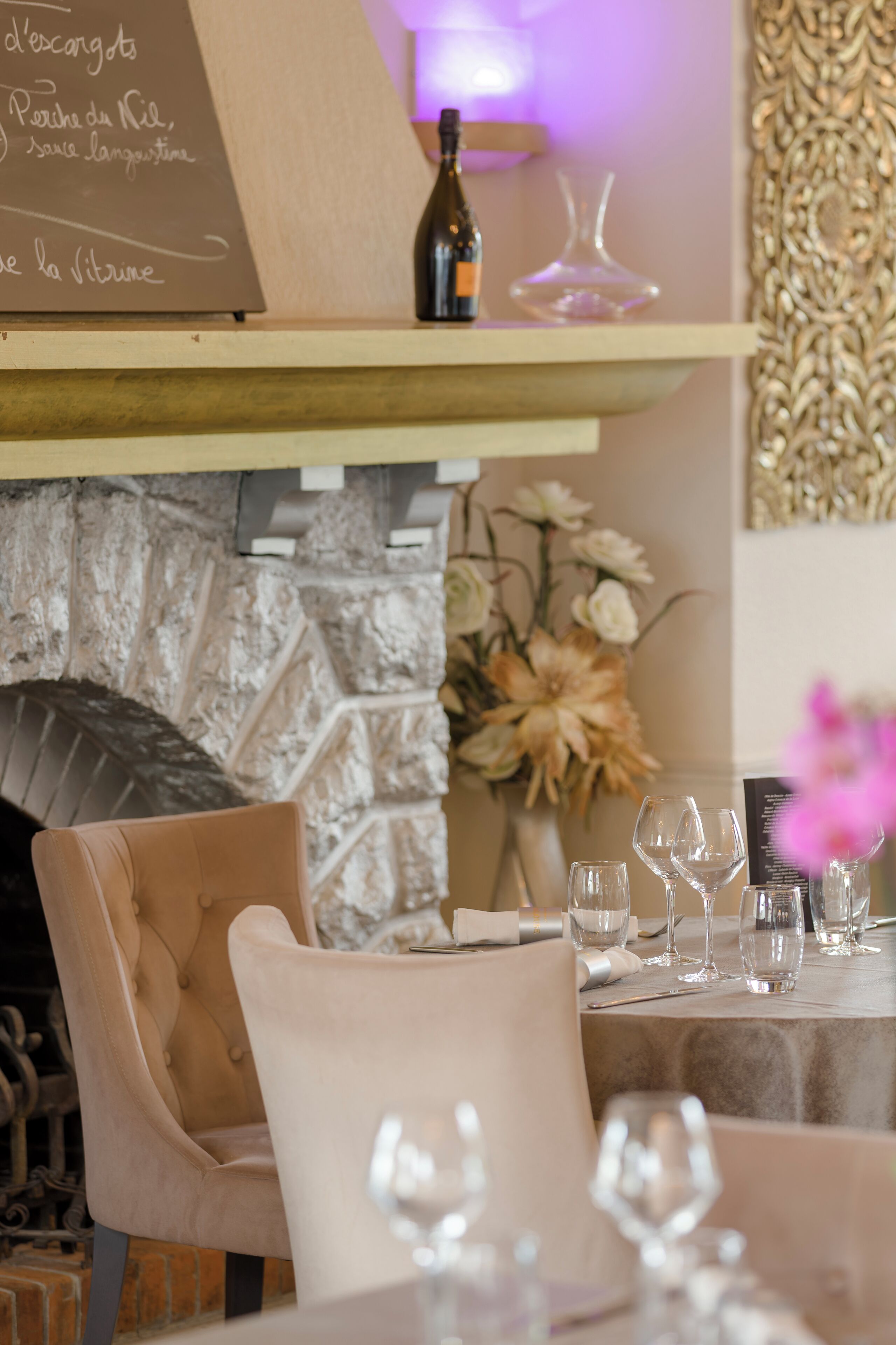 A restaurant interior with a stone fireplace, a table set with wine glasses, and a menu board.