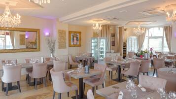 Un restaurante con varias mesas y sillas, candelabros y cuadros en las paredes.