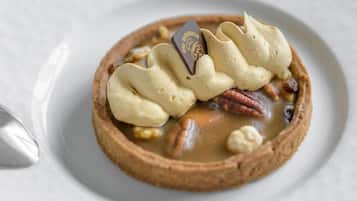 Un postre con crema batida, nueces pecanas y un trozo de chocolate en un plato.
