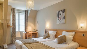 A hotel room with two beds, a desk, a chair, a hanging light fixture, and a painting on the wall. - Hôtel Le Vouglans (Orgelet)