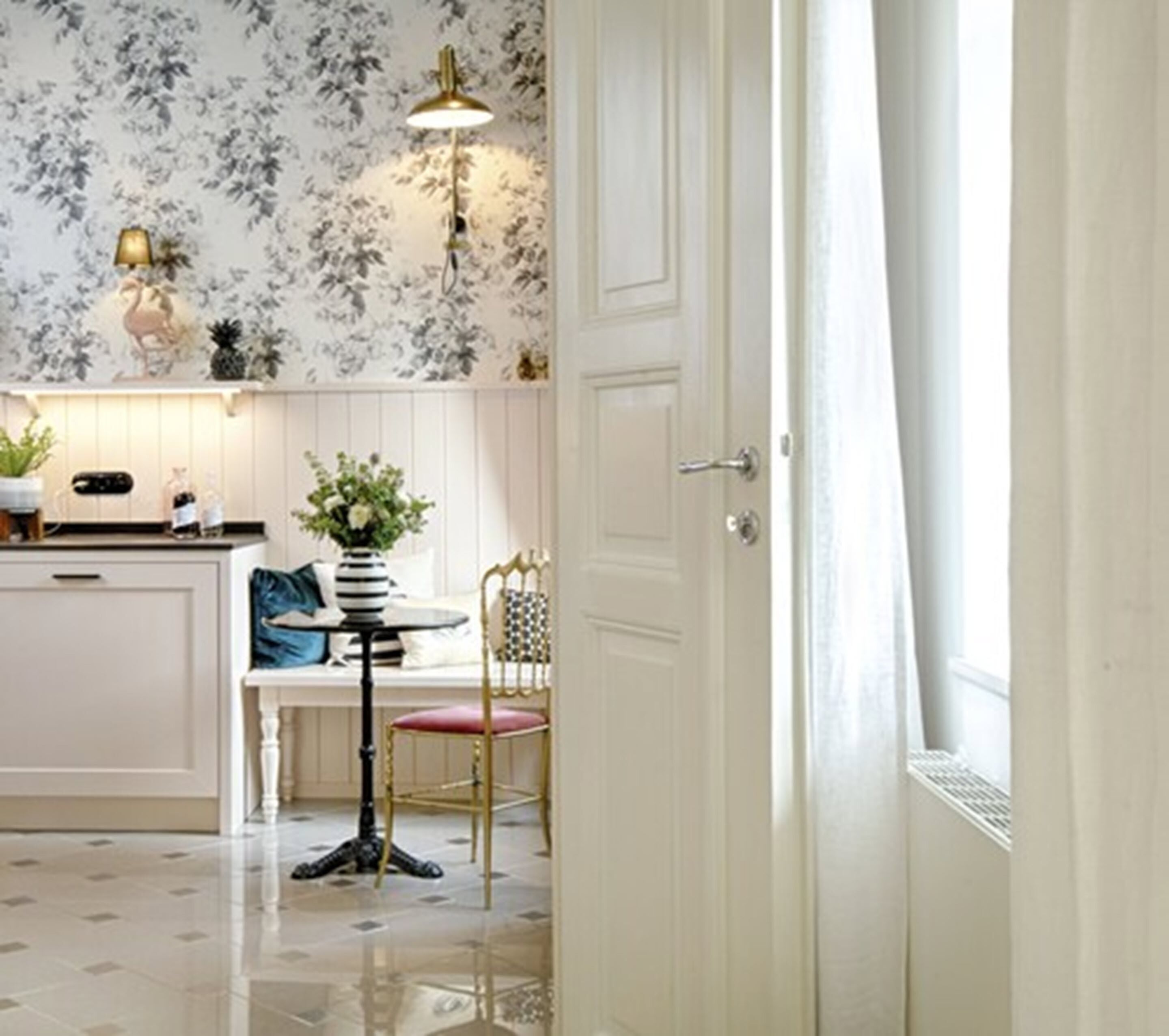 Een keuken met een witte kast, een eettafel met een stoel, een vaas met bloemen en een hanglamp.