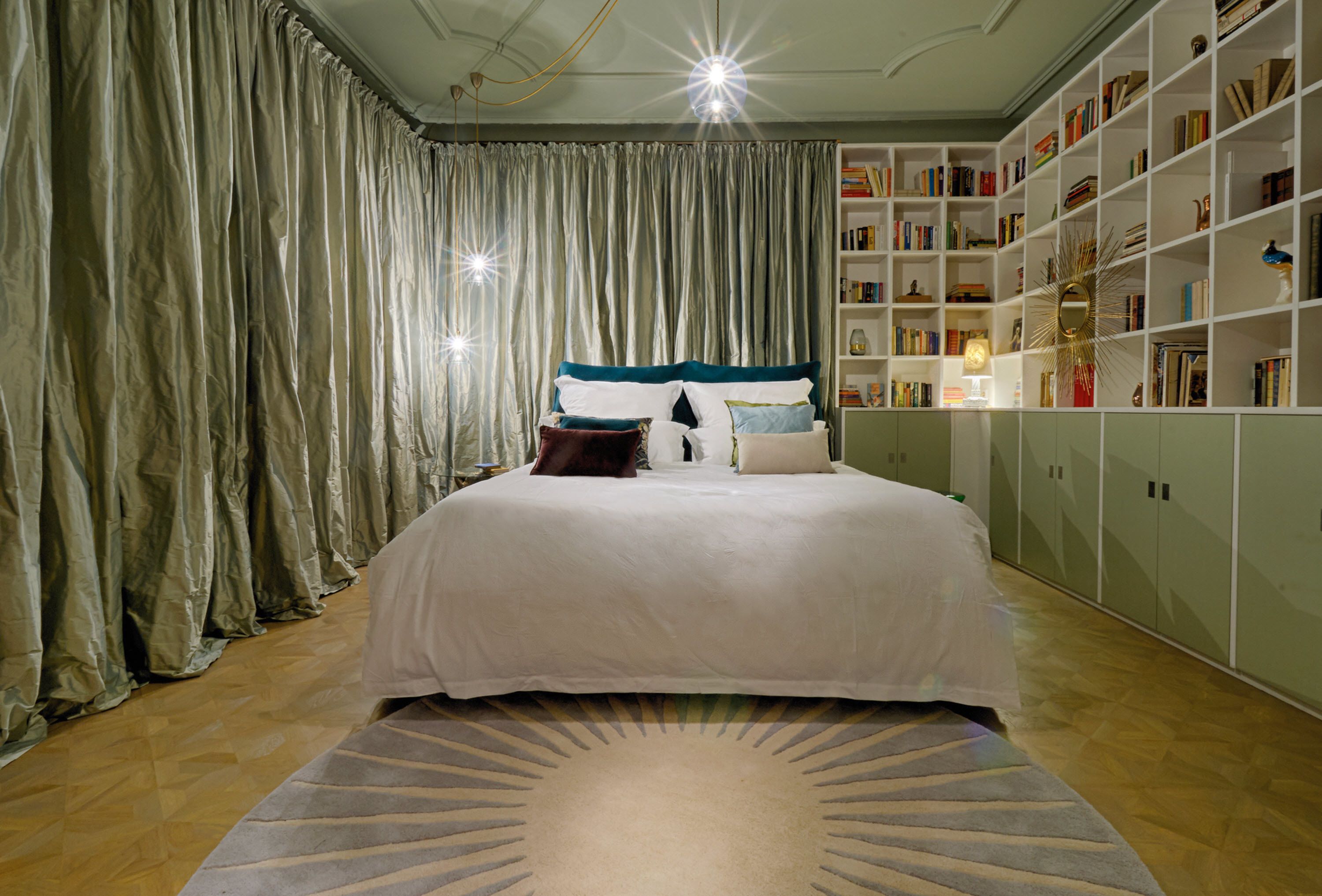 A bedroom with a large bed, a bookshelf, and a patterned rug.